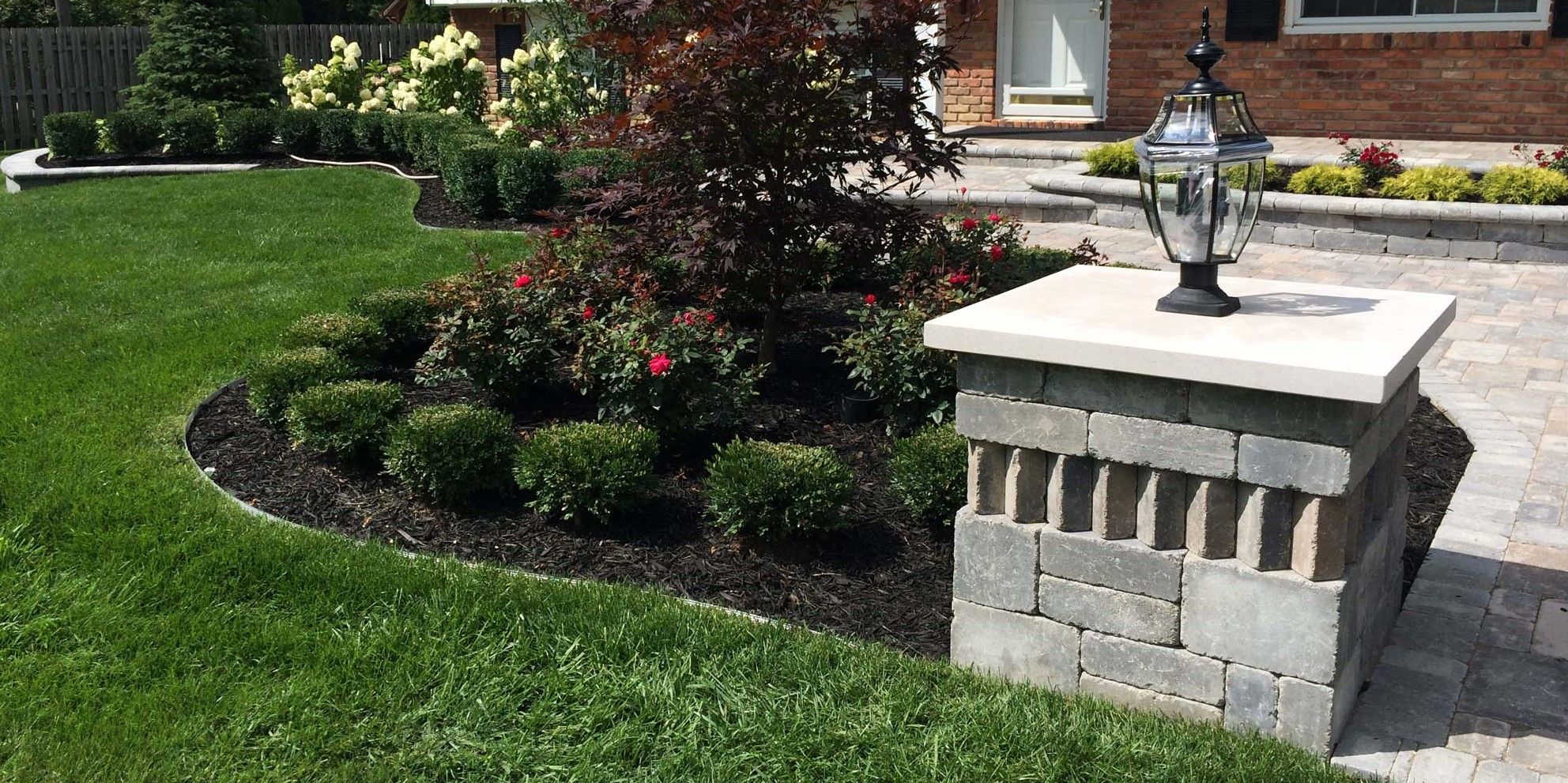 Brick pillar with lamp, paver walkway, and flower bed.