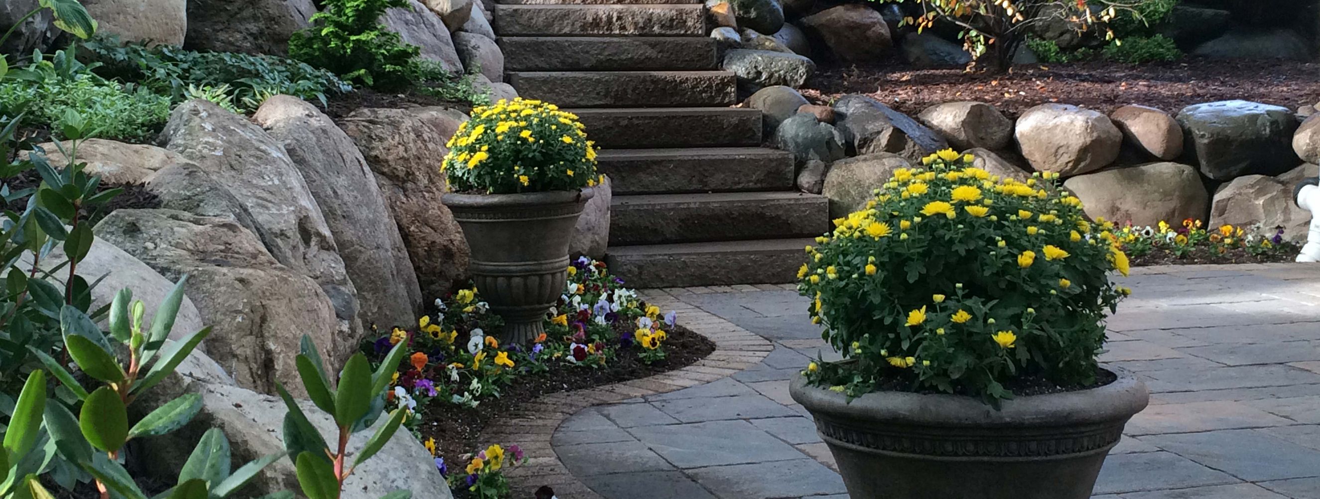 Brick patio, stone stairs, and rock walls with flowering planters.